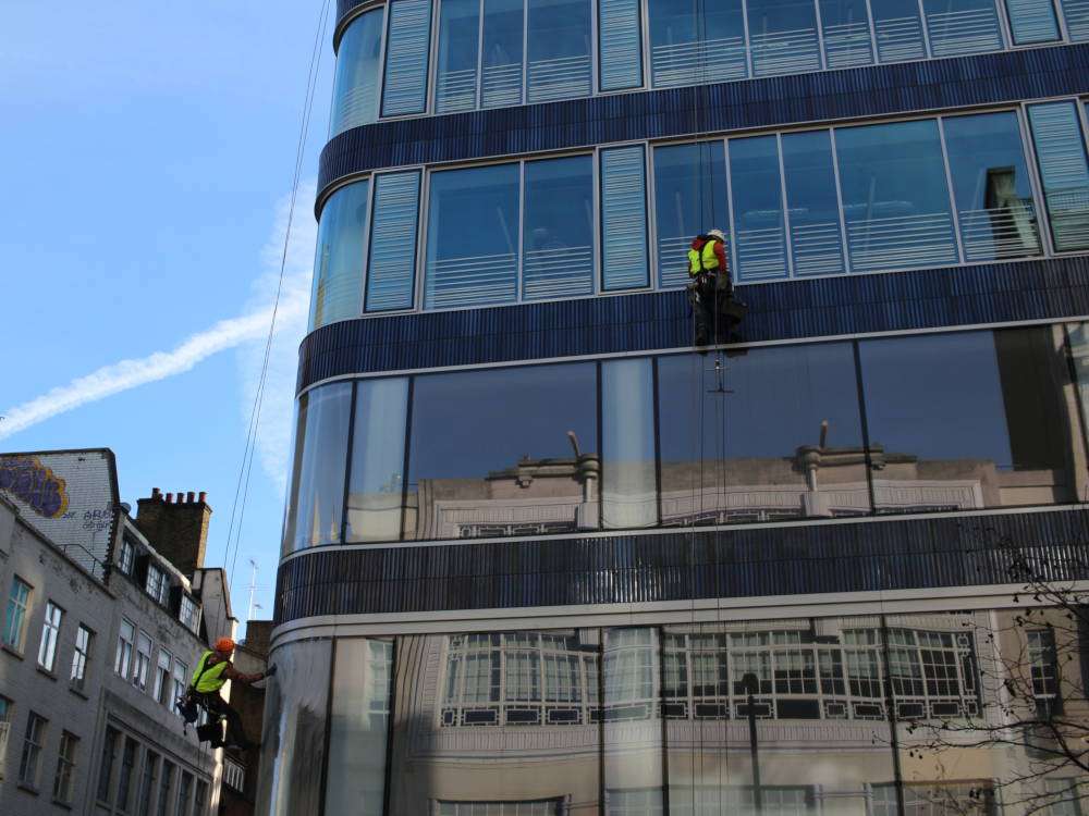 Two rope-access cleaners working on a high-level glass building